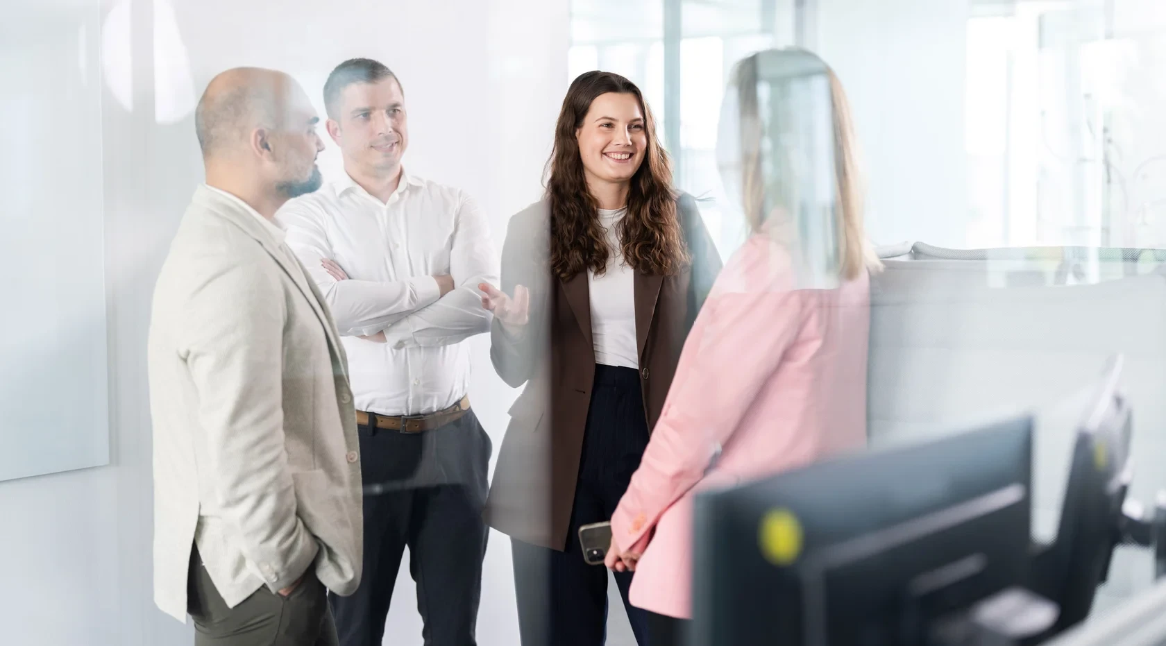 Business-Talk im offenen Büro Vier Personen unterhalten sich stehend in einem modernen Büro mit Glaswänden und Business-Outfits.