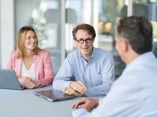 Business meeting by the window seat. Three people in a meeting with laptops in a bright office with large windows.