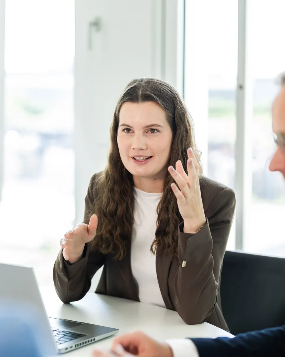 Strategiemeeting mit Fokus auf Erfolg Drei Personen im Gespräch an einem Tisch mit Laptop und Whiteboard im modernen Büro.